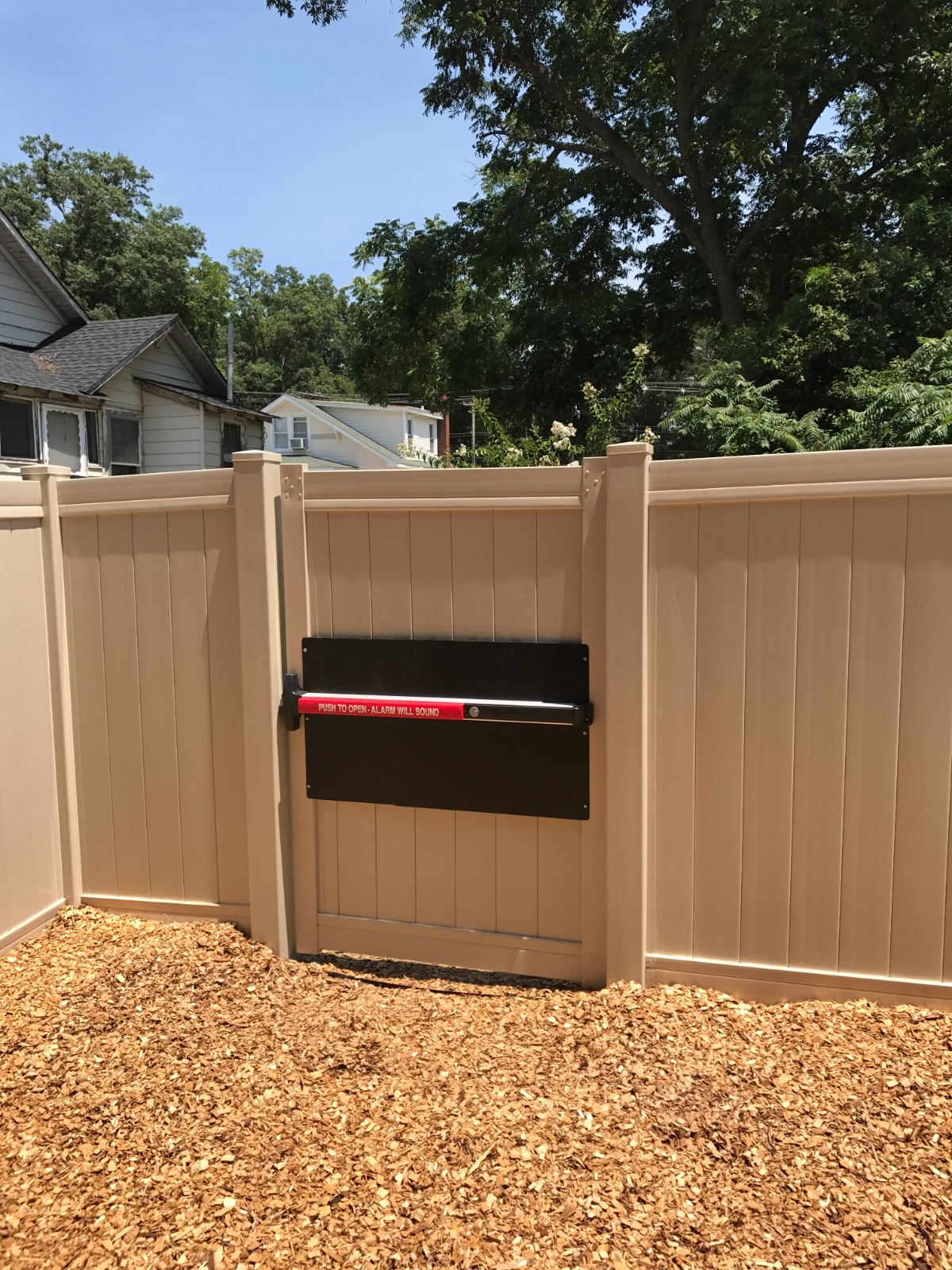 Panic hardware on 6-foot high tan vinyl privacy fence gate at Mission Baptist Church