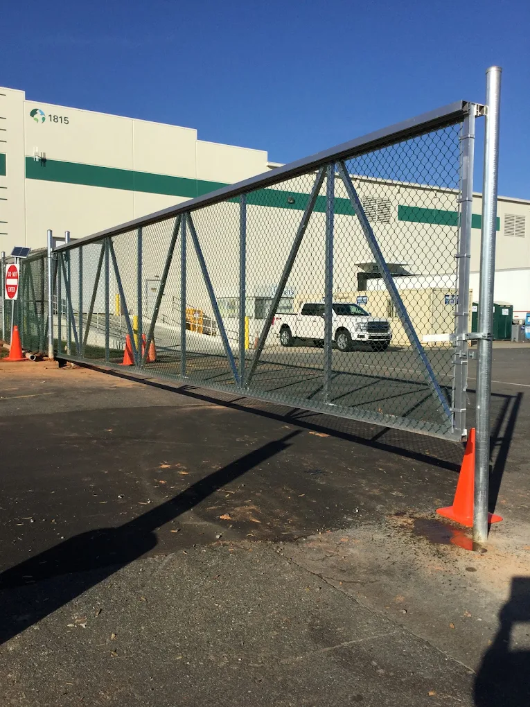 Metal chain-link gate with steel frame and orange traffic cones at industrial facility entrance