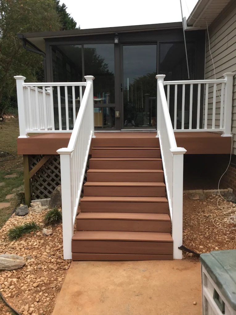 Composite deck with white railings and brown composite stairs leading to modern home with black framed glass doors