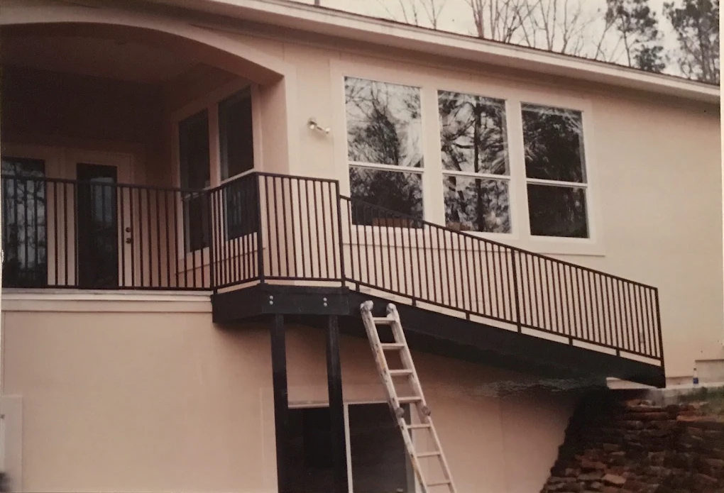 Modern elevated deck with black metal railing attached to pink house with large windows