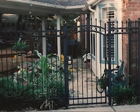 Black metal gate entrance with brick building and potted plants visible beyond