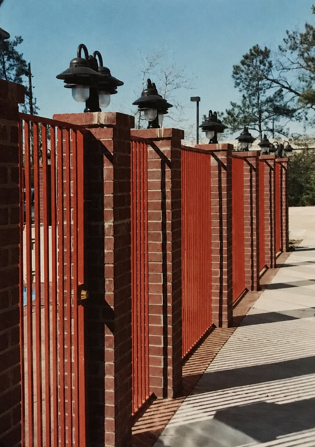 Red metal fence with brick pillars and black lamp post tops in a row